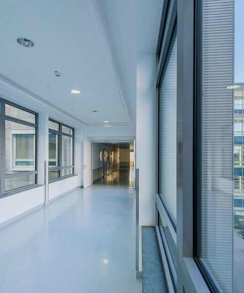 Heller, moderner Flur mit großen Fenstern und glänzendem Boden in einem Büro- oder Klinikgebäude.