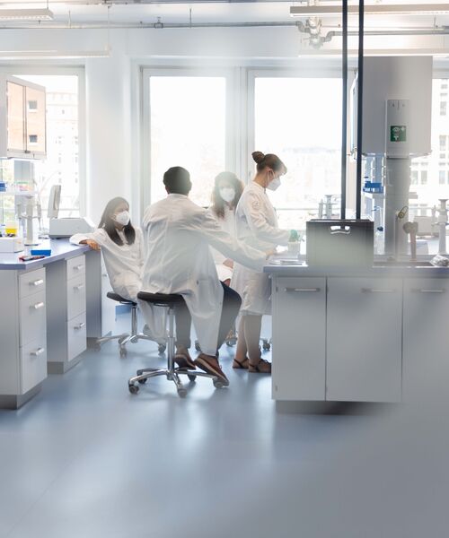 Gruppe von Labormitarbeitenden in Schutzkleidung arbeitet gemeinsam in einem hellen Forschungslabor.