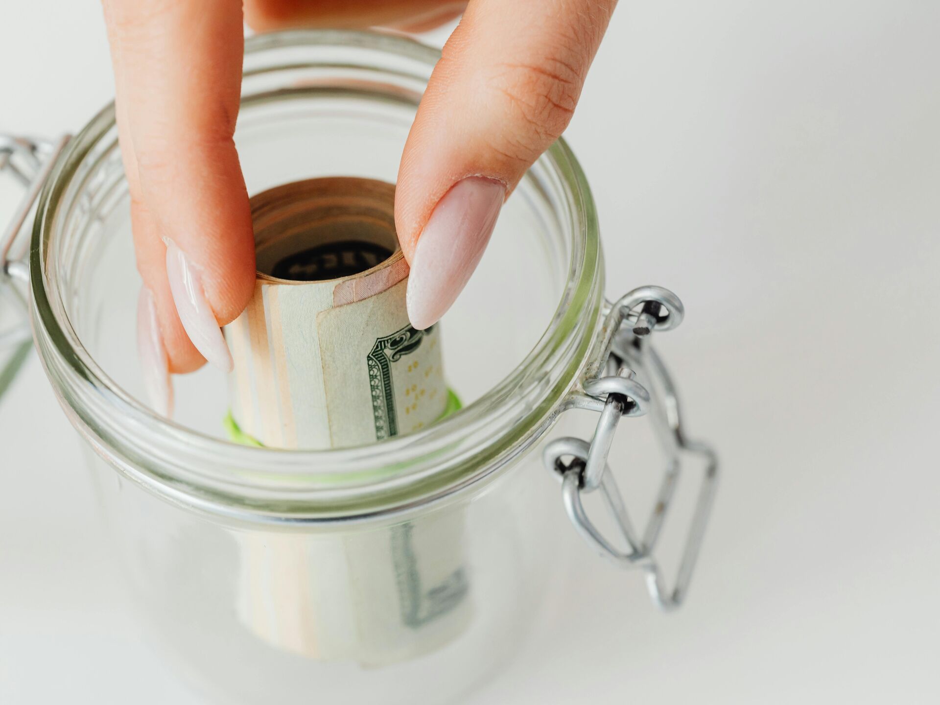 Hand legt eine zusammengerollte Geldscheinnote in ein Glasgefäß.