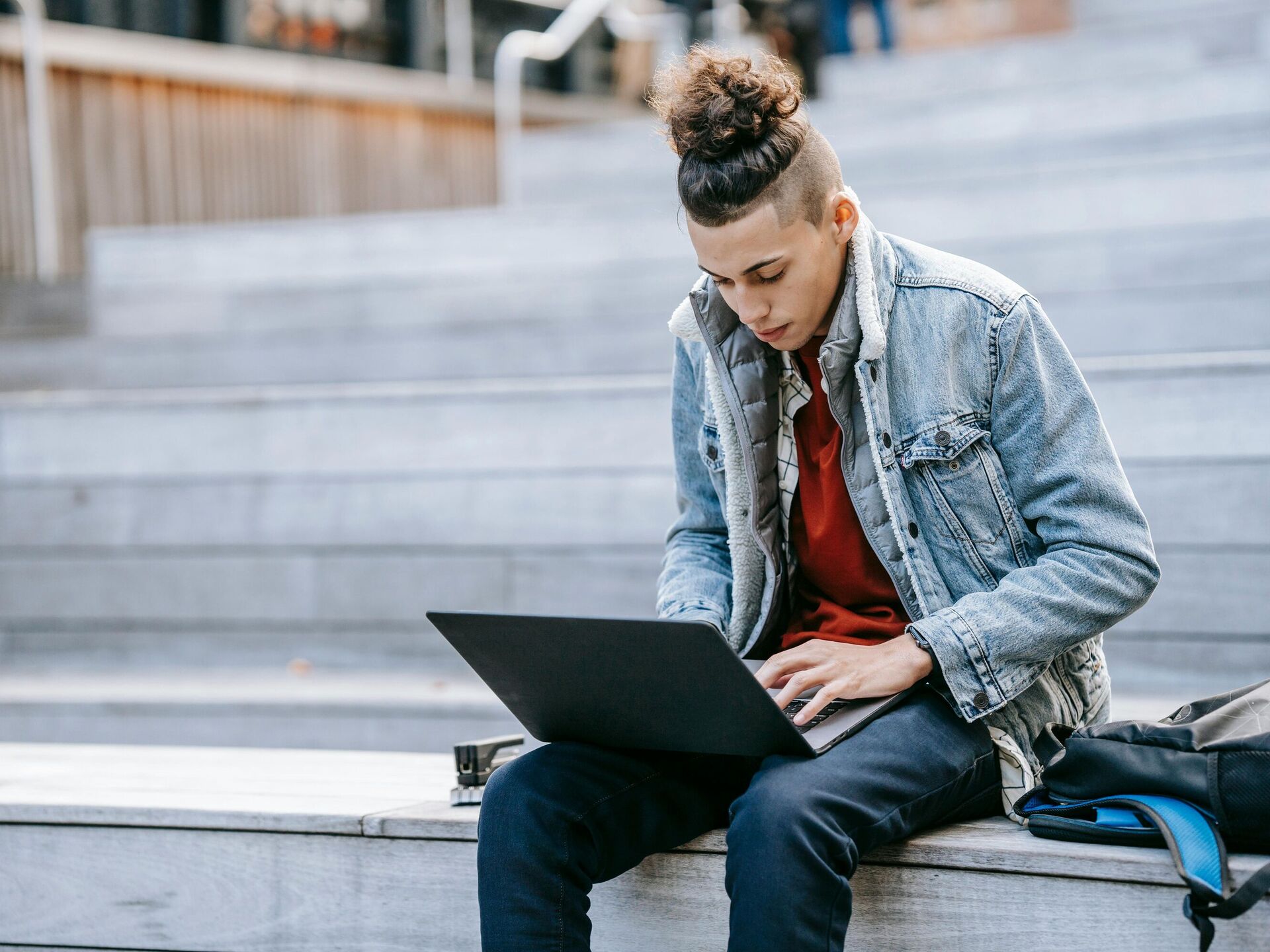 Junger Mann sitzt draußen auf Treppenstufen und arbeitet konzentriert an einem Laptop.