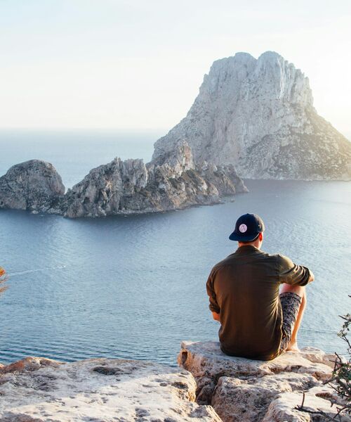 Person sitzt auf einem Felsen und blickt auf das Meer und eine vorgelagerte Insel.
