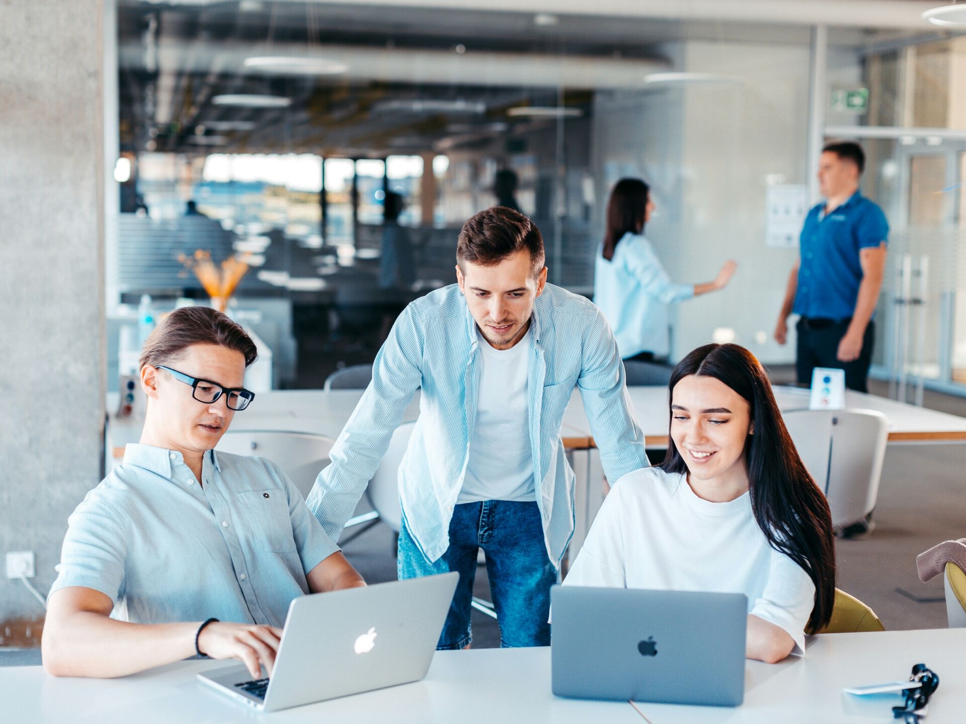 Drei junge Erwachsene arbeiten gemeinsam an Laptops in einem modernen Büro- oder Lernraum.