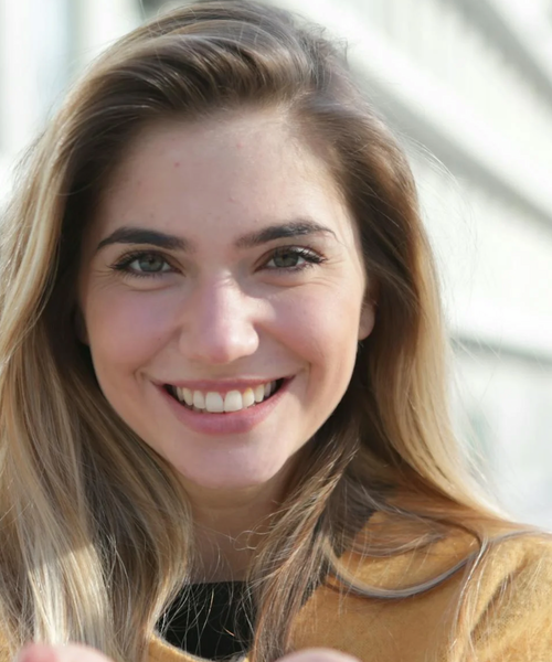 Porträt einer lächelnden jungen Frau im Außenbereich bei natürlichem Licht.