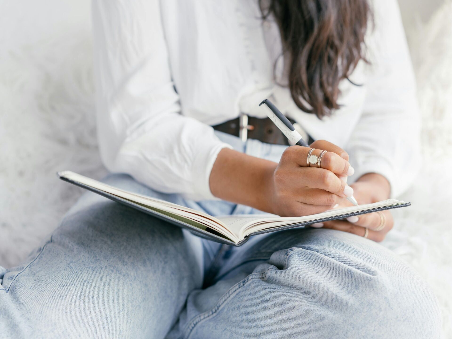 Person sitzt entspannt und schreibt mit einem Stift in ein geöffnetes Notizbuch auf dem Schoß.