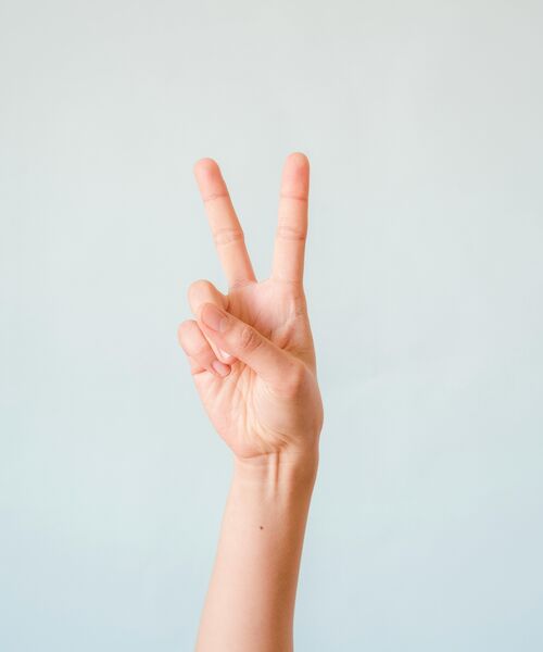 Hand zeigt ein erhobenes Peace-Zeichen vor hellem Hintergrund.