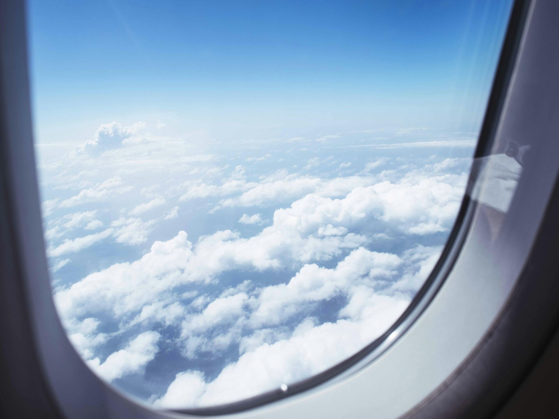 Blick aus einem Flugzeugfenster auf weiße Wolken und blauen Himmel.