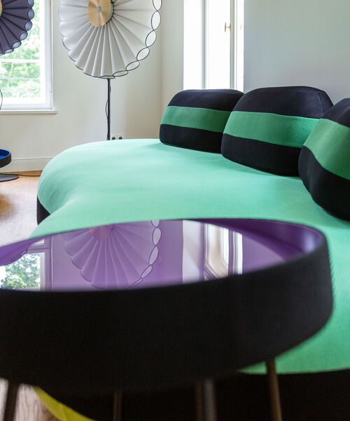 Modernes Wohnzimmer mit grün-schwarzem Designersofa und reflektierendem lilafarbenem Beistelltisch.