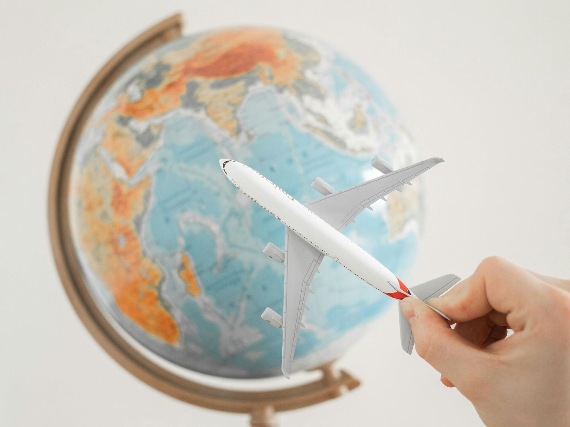 Hand hält ein Modellflugzeug vor einem Globus, der auf einem Holztisch steht.