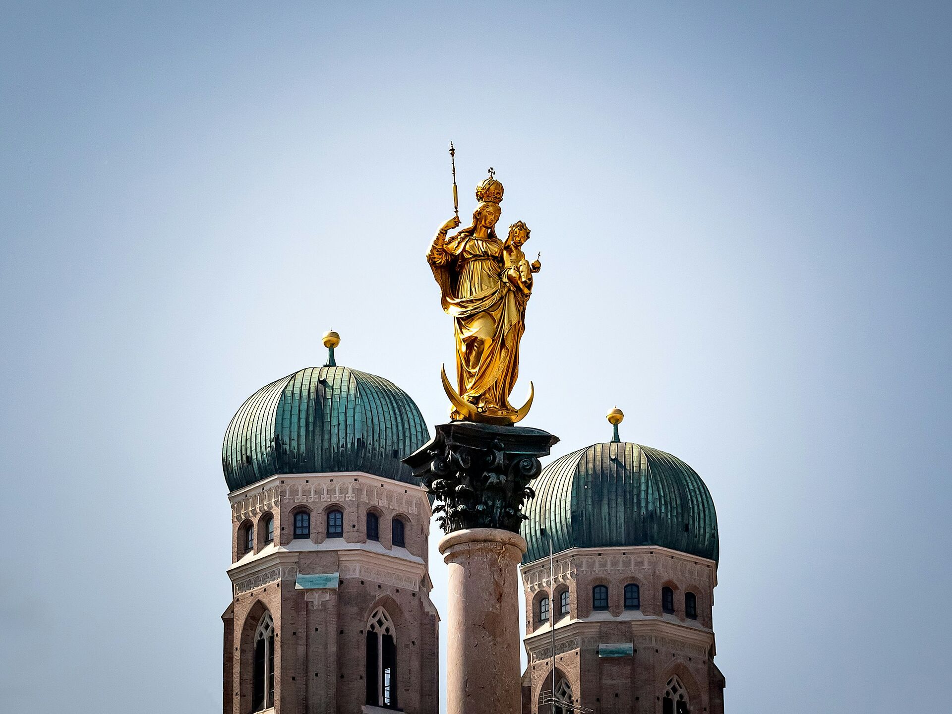 Goldene Marienstatue auf der Mariensäule vor den markanten Zwiebeltürmen der Münchner Frauenkirche.