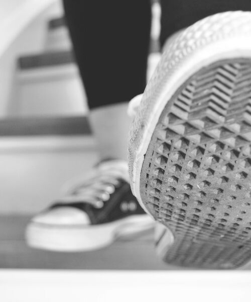 Nahaufnahme einer Person, die eine Treppe hinaufgeht, mit Fokus auf die Sohle eines Sneakers.