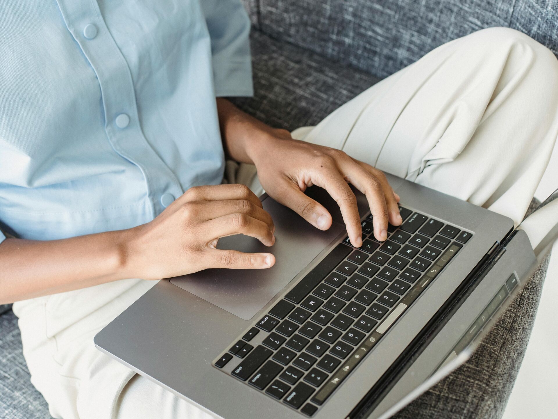 Nahaufnahme von Händen, die auf einem Laptop auf dem Schoß tippen.