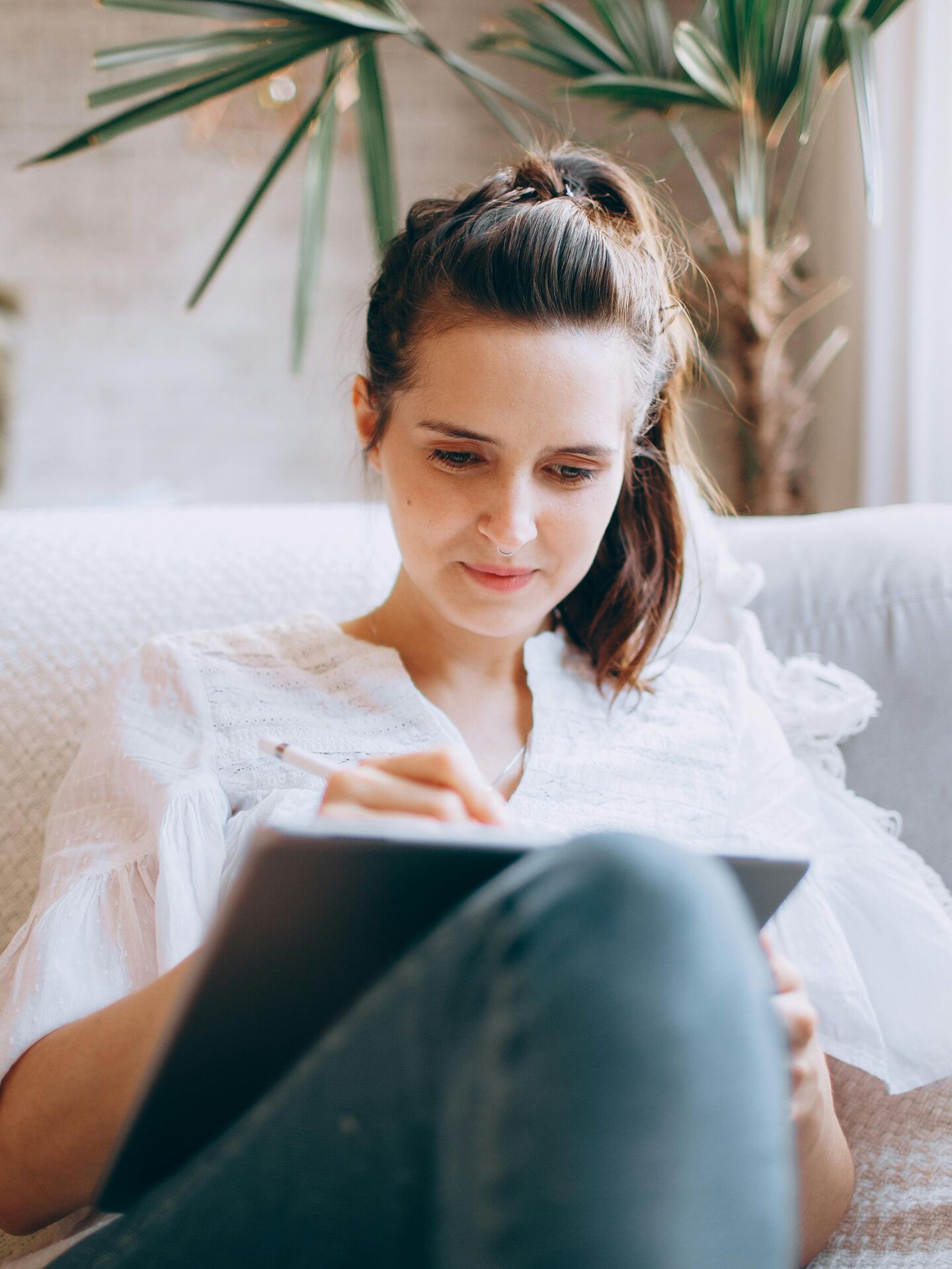 Frau sitzt entspannt auf einem Sofa und arbeitet konzentriert mit einem Tablet und Stylus.