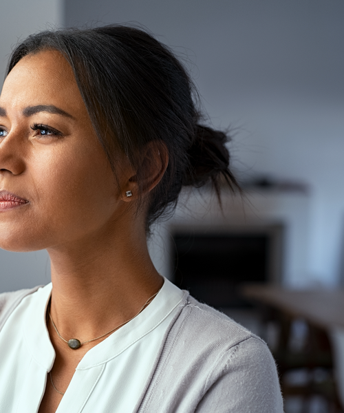 Porträt einer nachdenklich blickenden Frau in heller Kleidung in einem Innenraum.