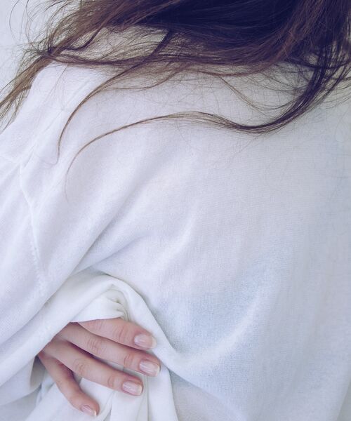 Detailaufnahme einer Person in einem weißen Pullover, deren Hand locker den Stoff greift.