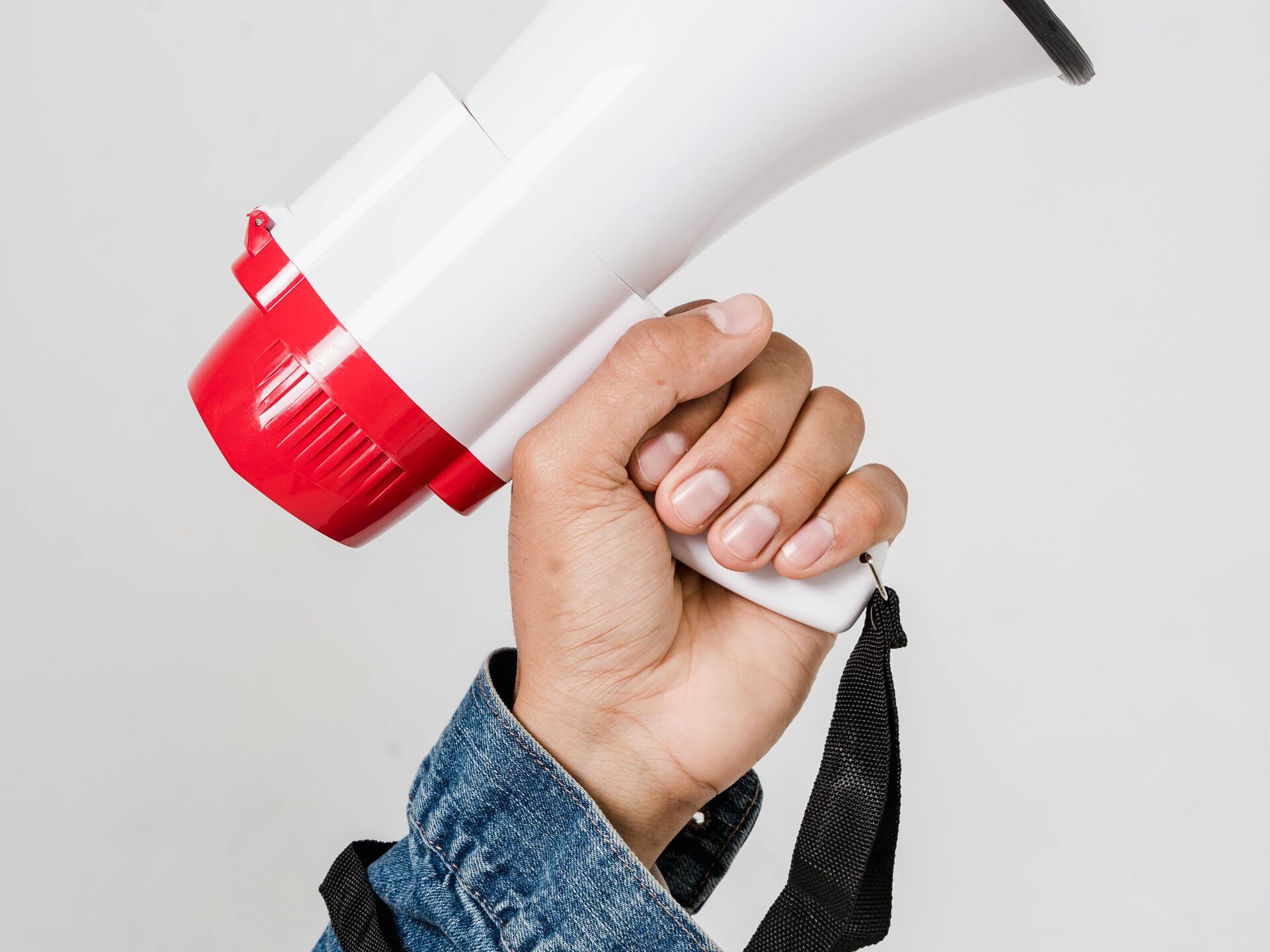 Hand in Jeansjacke hält ein weiß-rotes Megafon vor hellem Hintergrund.