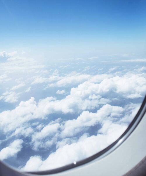 Blick aus einem Flugzeugfenster auf weiße Wolken und blauen Himmel.
