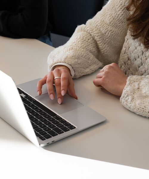 Person arbeitet an einem Laptop in heller Umgebung, Fokus auf den Händen und der Tätigkeit am Computer.