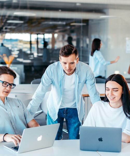 Drei junge Erwachsene arbeiten gemeinsam an Laptops in einem modernen Büro- oder Lernraum.